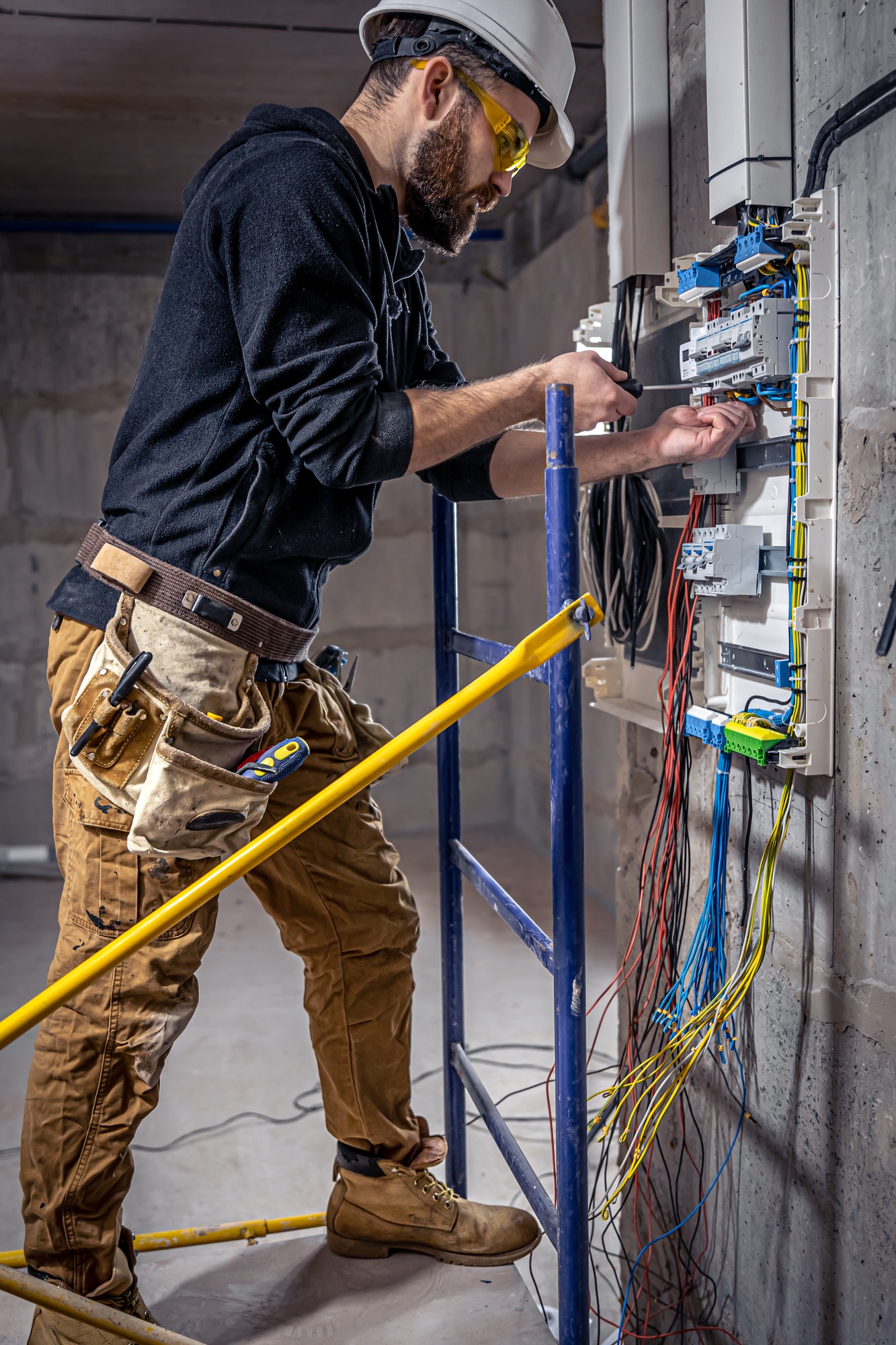 A male electrician works in a switchboard with an electrical connecting cable