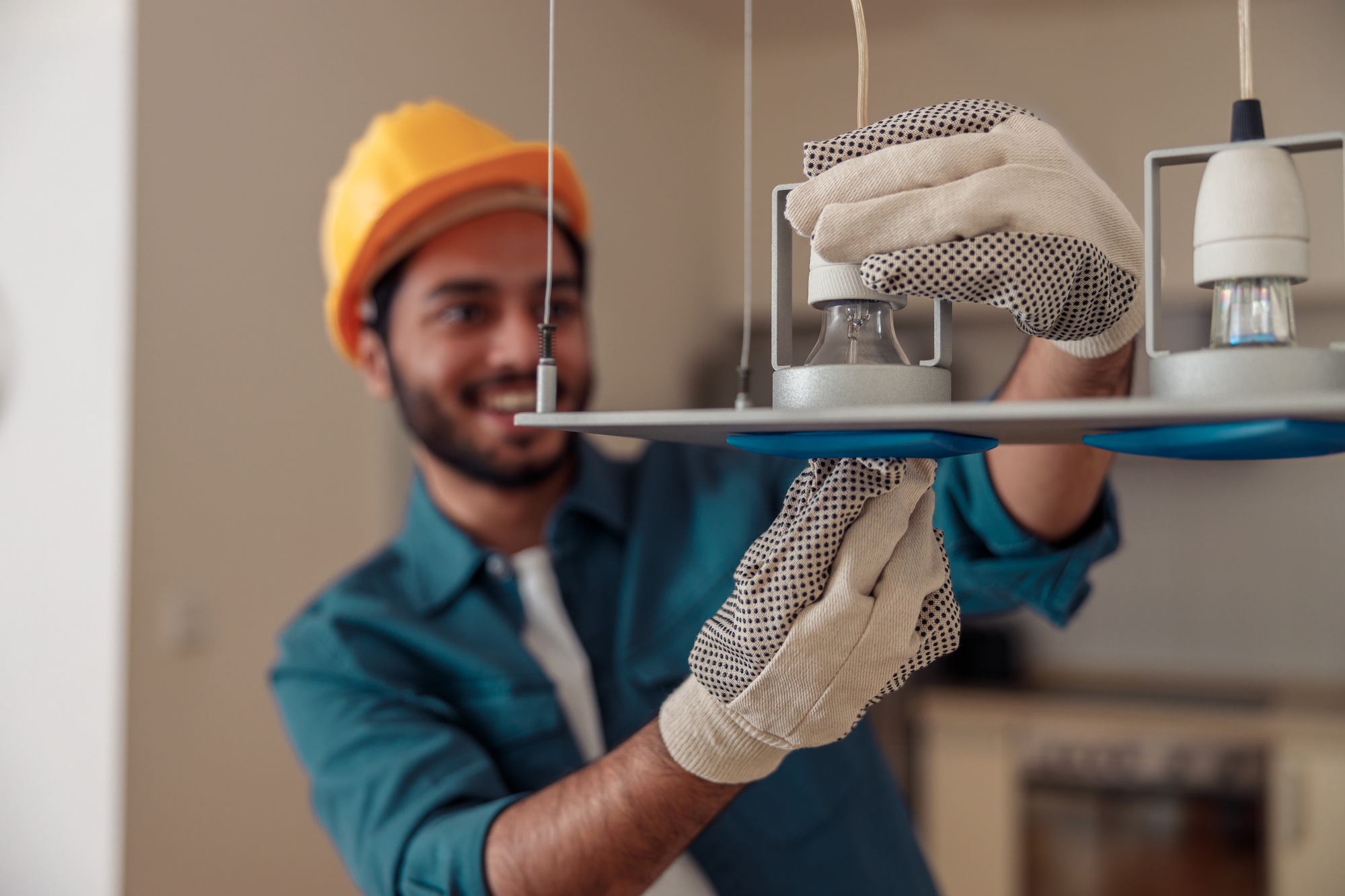 Electrician in uniform installing light bulbs into a chandelier
